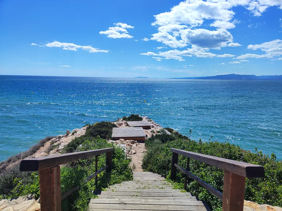 Escala de fusta que baixa a la Punta Grossa de Salou, amb el mar Mediterrani blau i núvols al fons
